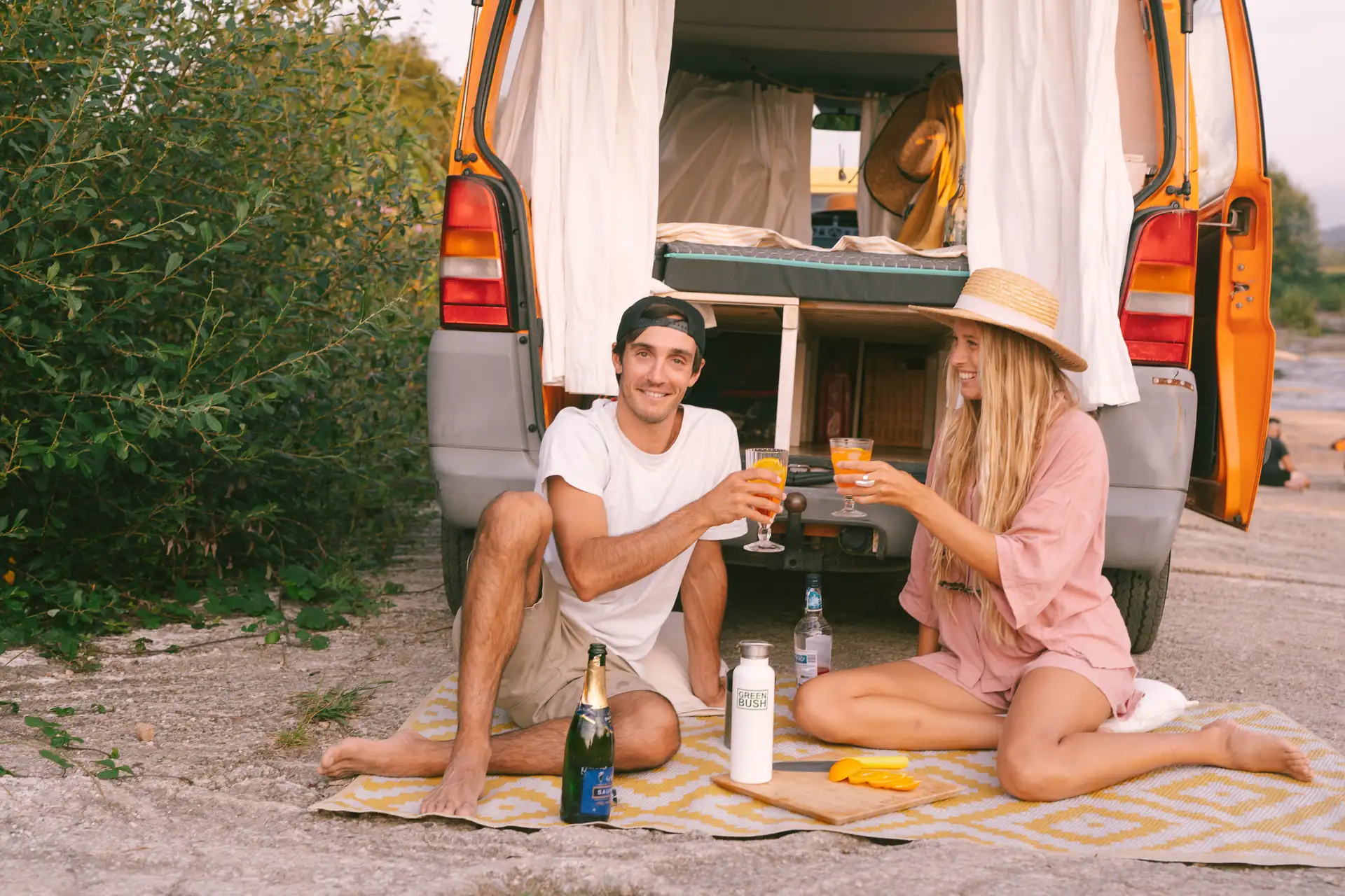 Lifestyle, junges Surfer Paar macht ein PickNick vor orangenem Van, Abendstimmung