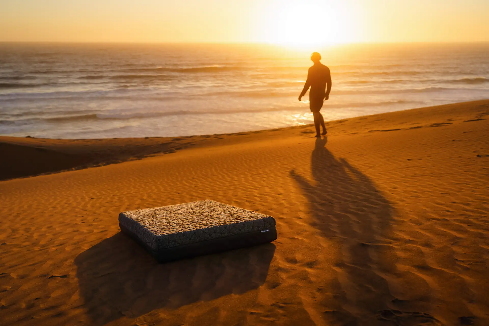 Mood, Vanmade Matratze liegt in der Wueste, Mann geht im Hintergrund Richtung Meer