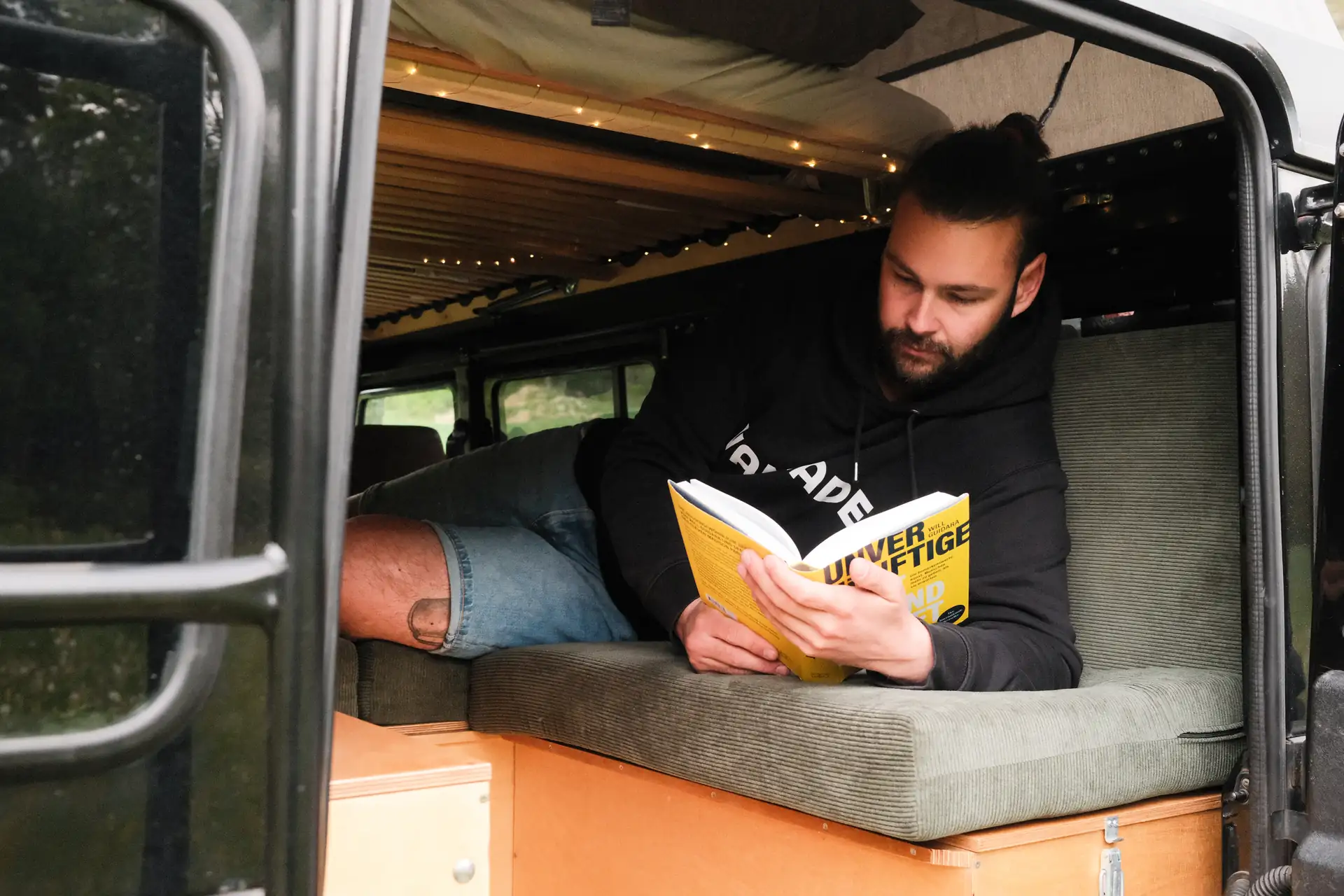 Paul liegt in Nahaufnahme auf seinen Cord Polstern in seinem Defender und liest